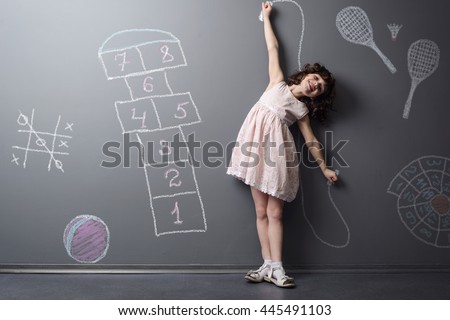 Child loves to be active and smiles while doing sports. Depicted childish favorite games like hopscotch, badminton and jumping rope on the neutral background in the studio.