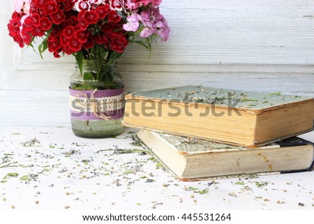Cute composition with old books in shabby grey cover and bouquet of flowers in a glass top decorated with lace on white wooden background. Vintage objects. Romantic decor elements. Pure white color
