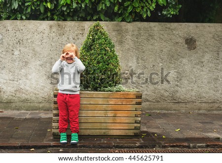 Fashion portrait of adorable toddler boy wearing grey sweatshirt, red trainings and green shoes. Kid pretending taking pictures with his hands