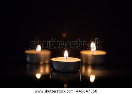 Candles in the dark. Round candle. floating candles in an aluminum sleeve. aluminium burning tea candle Isolated on a black background. Cozy burning candles. Low light atmosphere
