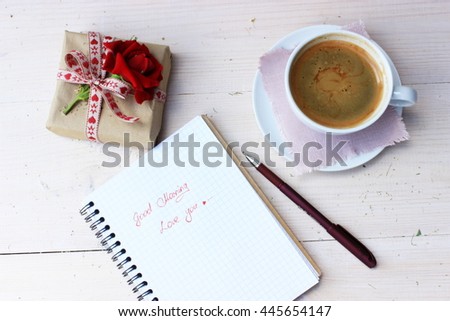 Good morning message for love person writing with red pen in a notebook, small cute gift box decorated with natural rose and cup of sweet tasty coffee. Romantic lifestyle. Floral decor