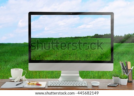 Conceptual image of a work space and computer desktop with green field and blue sky