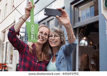 Women in front of shop holding open sign taking selfie with smartphone