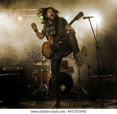 Rock band performs on stage. Guitarist, bass guitar and drums. The guitarist plays solo. Royalty-Free Stock Photo #445701640