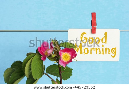 flower and piece of paper with text "good morning" on the wooden table close-up. sunlight effect image