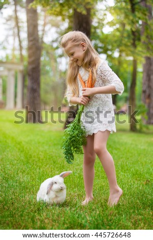 Little girl playing with white rabbit outdoor. Summer outdoor fun for children.