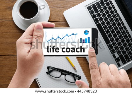 life coach message on hand holding to touch a phone, top view, table computer coffee and book