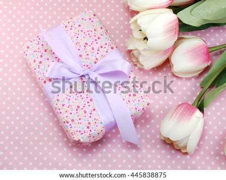 pink gift box with bow present and tulip artificial flowers on pink polka dot background