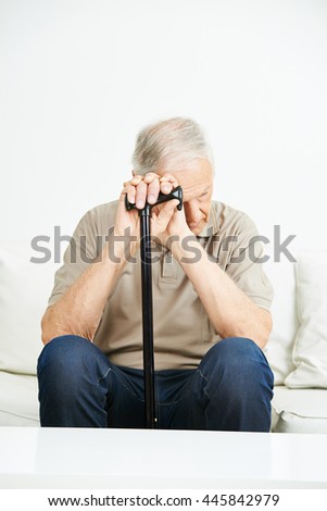 Sad senior man with cane sitting on a sofa