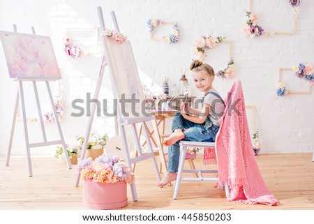 Little artist in denim overalls painting brushes on the easel in her studio Royalty-Free Stock Photo #445850203