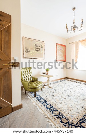Bright and spacious room in an elegant house, with a large oriental rug and a green leather quilted armchair