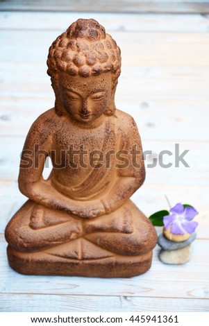 Close up of bronze brown stone Buddha statue with flowers in lotus position on old wooden planks