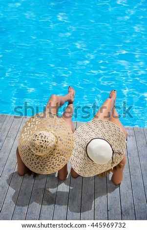 Two woman in a hat sitting on the edge of the swimming pool
