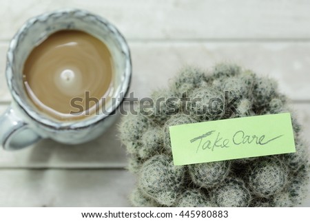 Port of cactus, hot coffee and paper note with word " take care "  on table. Selective focus.