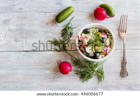 Healthy diet food: vegan vegetable salad with fresh cucumbers, radish, green onion, black olives, dill and feta cheese. In white ceramic bowl on light wooden background. 