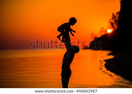Father throwing his kid up in the air on the beach, son at sunset
