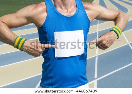 Brazilian athlete in Brazil colored wristbands pointing at blank race bib standing in front of the running track