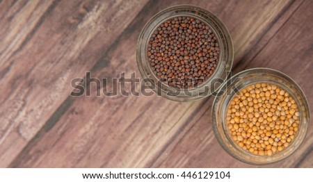 Yellow and brown indian mustard seed in mason jar over wooden background