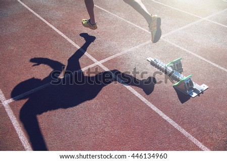 Abstract view of athlete in gold shoes sprinting from the starting line blocks of a race on a red running track 