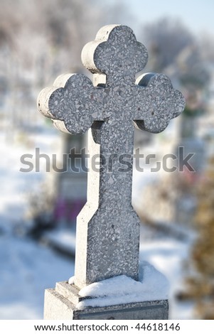 Stone cross on a cemetery covered with snow