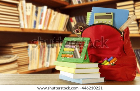 Backpack with school supplies on blurred library background