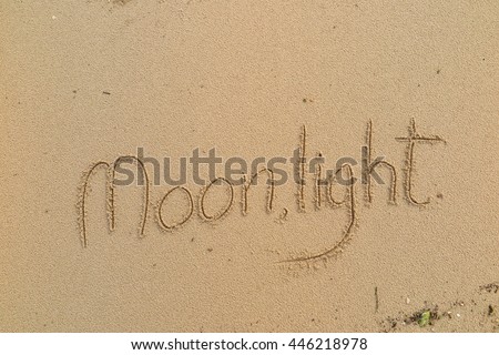 written words "Moonlight" on sand of beach