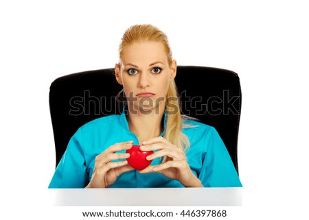 Worried female doctor or nurse sitting behind the desk and holding heart model