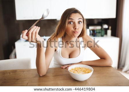 Picture of attractive young girl eating cornflakes with milk at kitchen and making fun