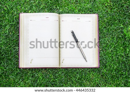 Day of knowledge and business topic: notebook and pen lie on the green grass top view