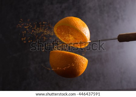 Knife and orange cut in half are frozen in mid air on a black background Royalty-Free Stock Photo #446437591