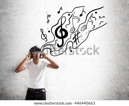 Stylish african american guy in shades and cap listening to music on concrete background with abstract sketch
