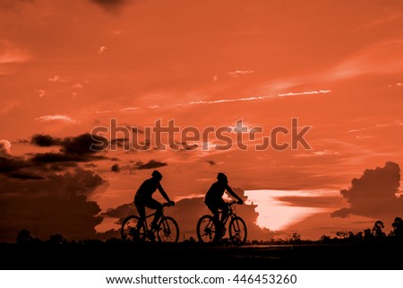 A man and a woman ride bicycle in the evening with warm tone sky,Silhouette background.