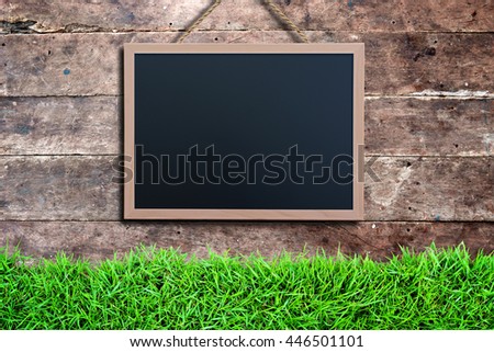 Blackboard hanging on dark grunge vintage wood wall panel background with green grass in front of. Empty and blank space for your text, copyspace or design.