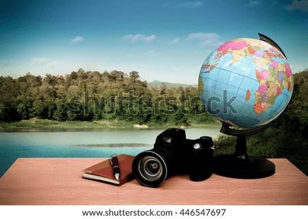 Globe ,notepad and camera on desk with lake and mountain background