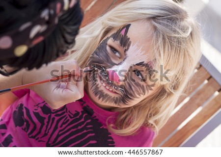 A little girl has her face painted as a cat
