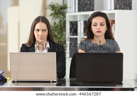 Front view of two angry businesswomen looking each other with hate working with laptops at office Royalty-Free Stock Photo #446567287