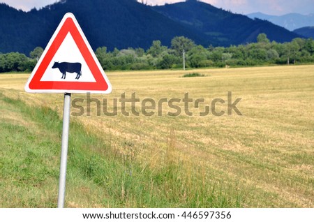 Cattle crossing traffic sign next to empty field.