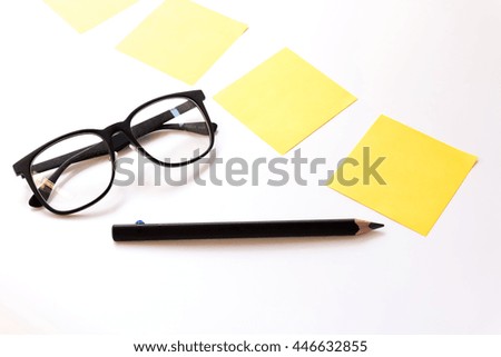 Yellow sticker note on a table with glasses and pencil.