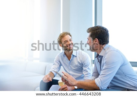 Smiling young businessman enjoying a positive conversation with a mature business partner in a modern space with large windows Royalty-Free Stock Photo #446643208