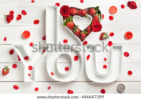 Decorative ceramics letters I Love You and Heart filled with strawberry and red roses on the white wooden background with candles for the romantic decor or St. Valentine's celebration