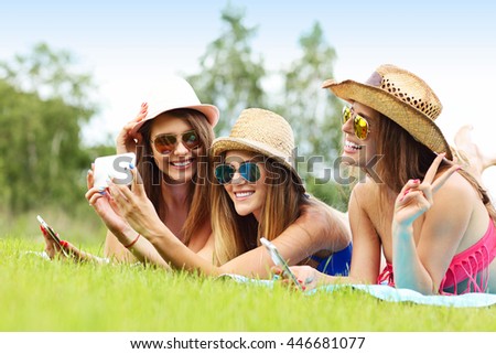Picture showing happy group of friends lying on the grass and taking selfie