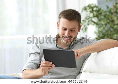 Happy man browsing in a tablet sitting on a couch at home