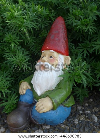 Garden Gnome with a red hat  in front of a green hedge 