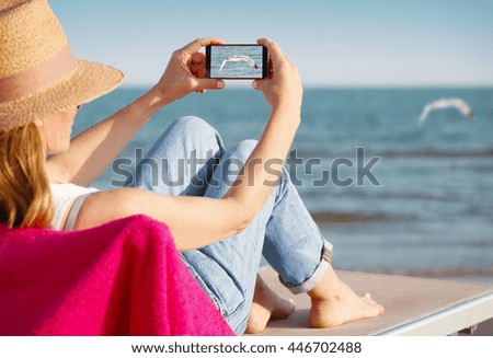 Portrait of relaxing woman sitting on sunbed at seaside and taking pictures with her mobile phone. 