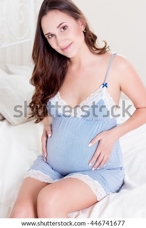 Happy pregnant woman sitting on the bed. A young pregnant woman is sitting in the bedroom. Pregnant woman relaxing.