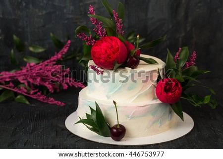 Dessert. Sponge cake with cherries, vanilla cream and flowers on the dark black background. White vintage pastel wedding cake decorated with flowers and cherry.