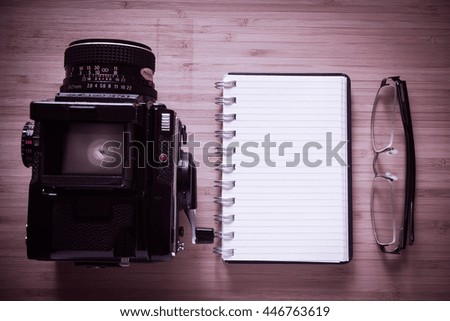 notebook with black pen, glasses, smart-phone and vintage medium format camera on old wooden desk. Top view. Free space for design