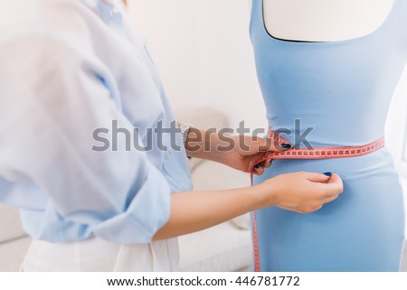 It is a picture where the main thing is concentrated on hands of a girl who makes fitting of dress on the mannequin. This picture is made in workshop studio.