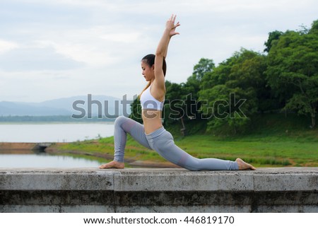 Young woman practicing yoga on the barrier of reservoir.