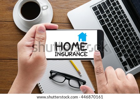 HOME INSURANCE message on hand holding to touch a phone, top view, table computer coffee and book